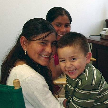 Two young girls and one toddler boy sibling smiling in an office