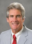 Closeup of a grey haired white man wearing a light grey suit with a white shirt and red tie