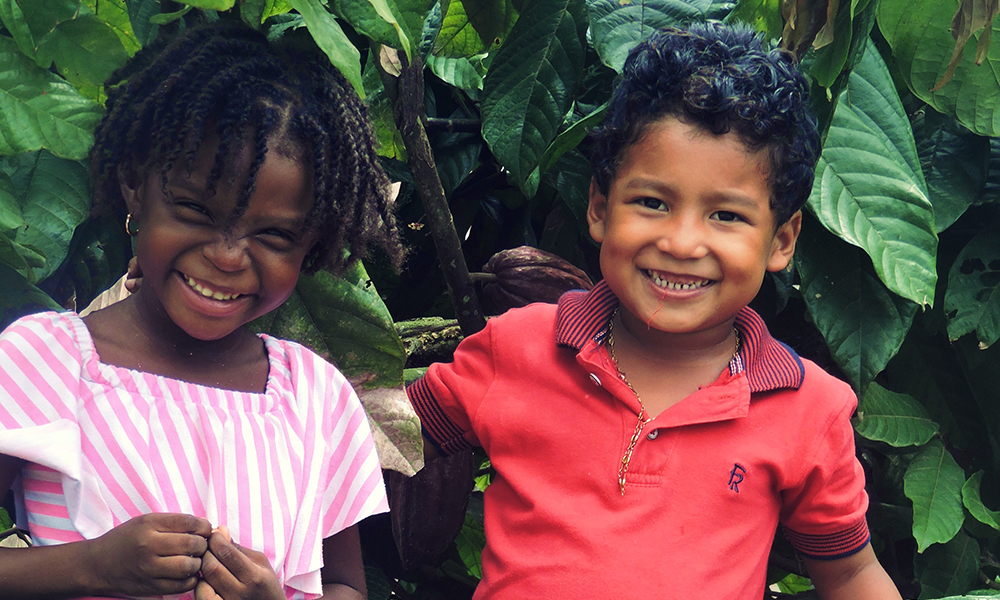 Young boy and young girl smiling in front of big green leaves