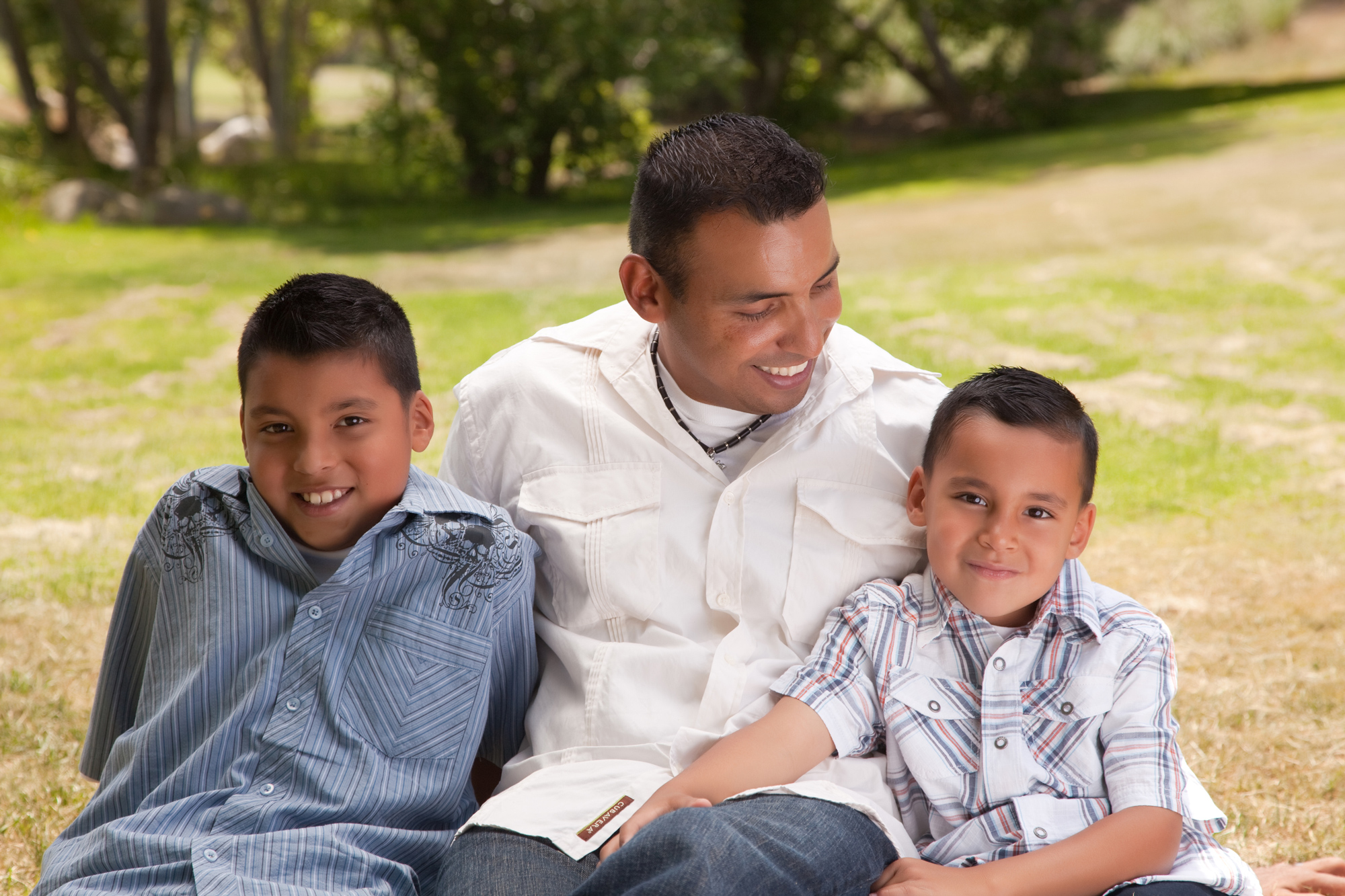 Young man sits on grass embracing two smiling young boys