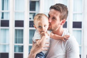 Young white man with short blonde-brown hair holds and kisses baby with blue eyes